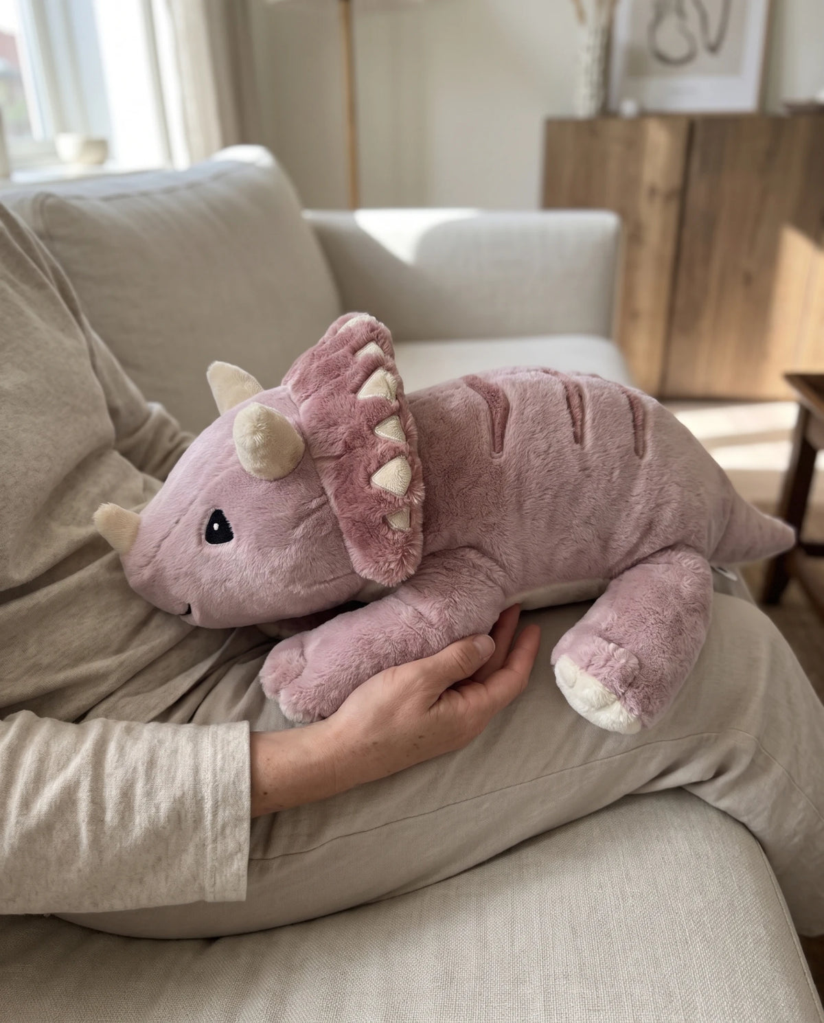 Weighted Dinosaur in Wild Rose resting in a lap on the sofa #Colour_Wild Rose