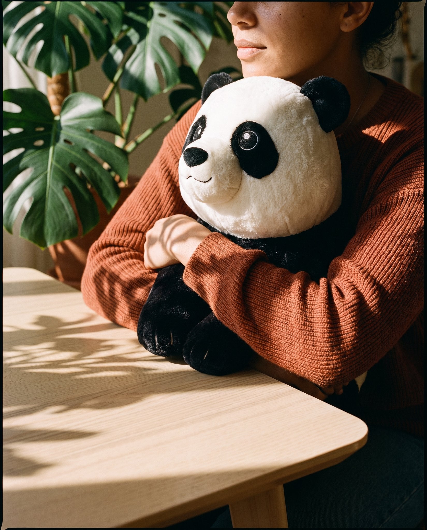Woman in a terracotta knit hugging the Brease weighted panda at a table