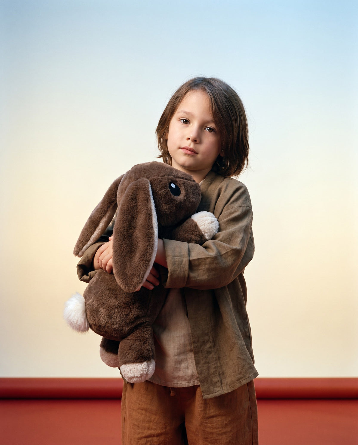 Studio portrait of a child holding the Brease Weighted Rabbit 5 lb in both arms, showing the 43 cm size next to a young child