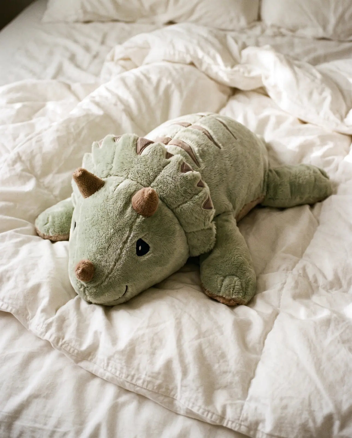 Weighted Dinosaur in Matcha, 2.3 kg, lying on an unmade white bed