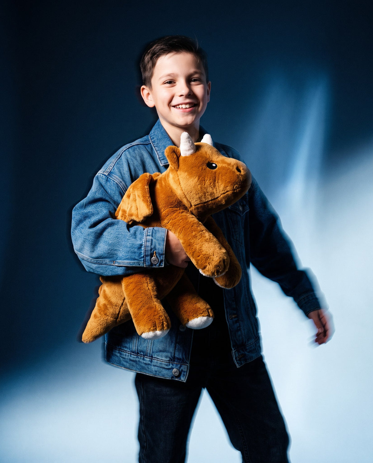 Smiling boy in a denim jacket carrying the Brease Weighted Dragon 5 lb weighted stuffed animal